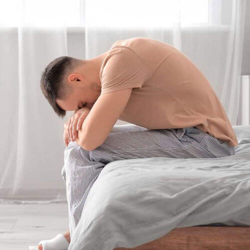 Homme confus au bord de son lit